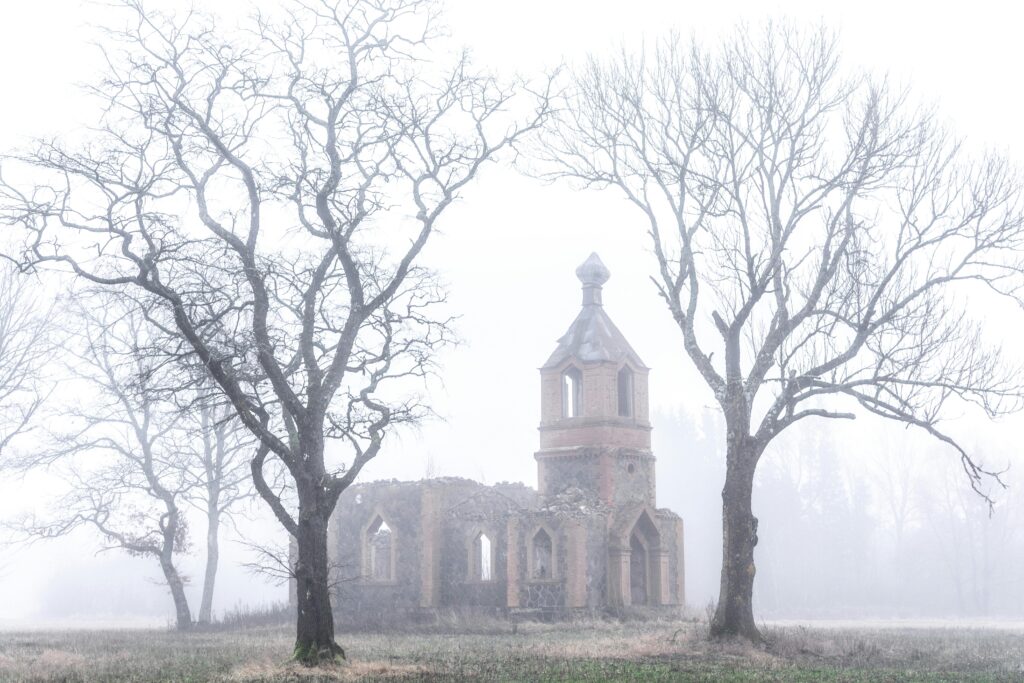 A foggy winter scene featuring a historic ruined church surrounded by bare trees in Kullamaa, Estonia.
